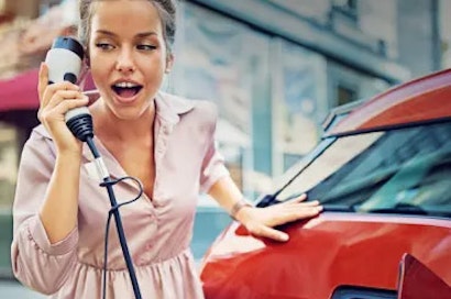 Frau benutzt das Ladekabel des Elektroautos als Telefon