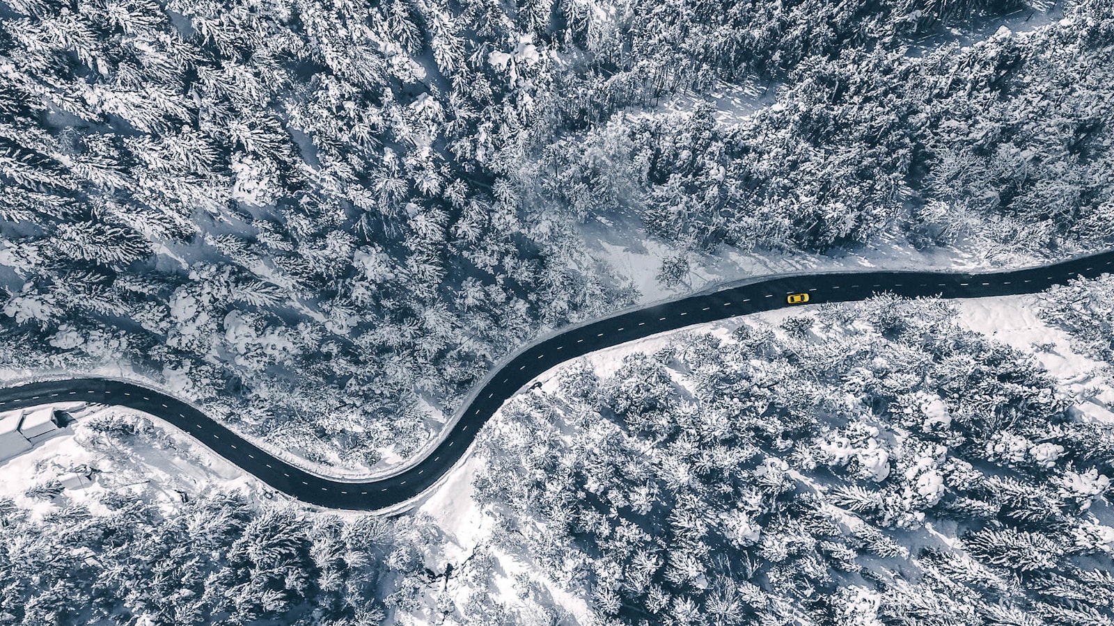 null Luftaufnahme eines gelbes Autos, das durch einen verschneiten Wald fährt